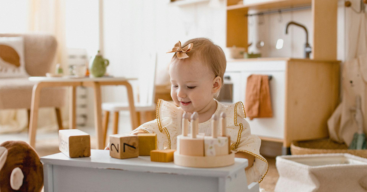 Mała dziewczynka bawi się przy drewnianej kuchence. Na pierwszym planie drewniany tort.